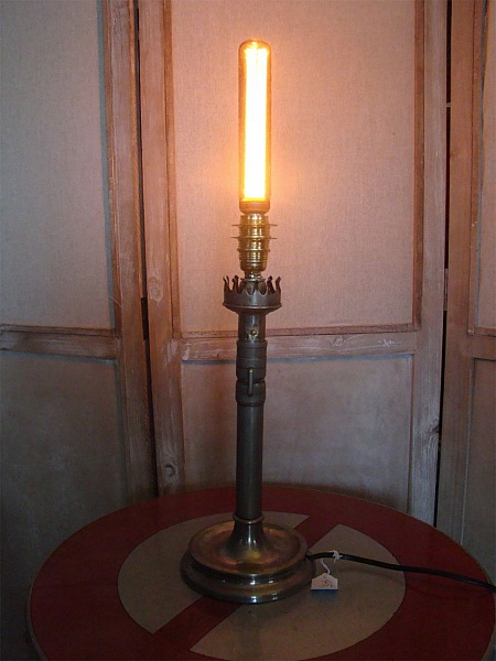 Lampe bougie ancienne en laiton avec ampoule Edison allumée.