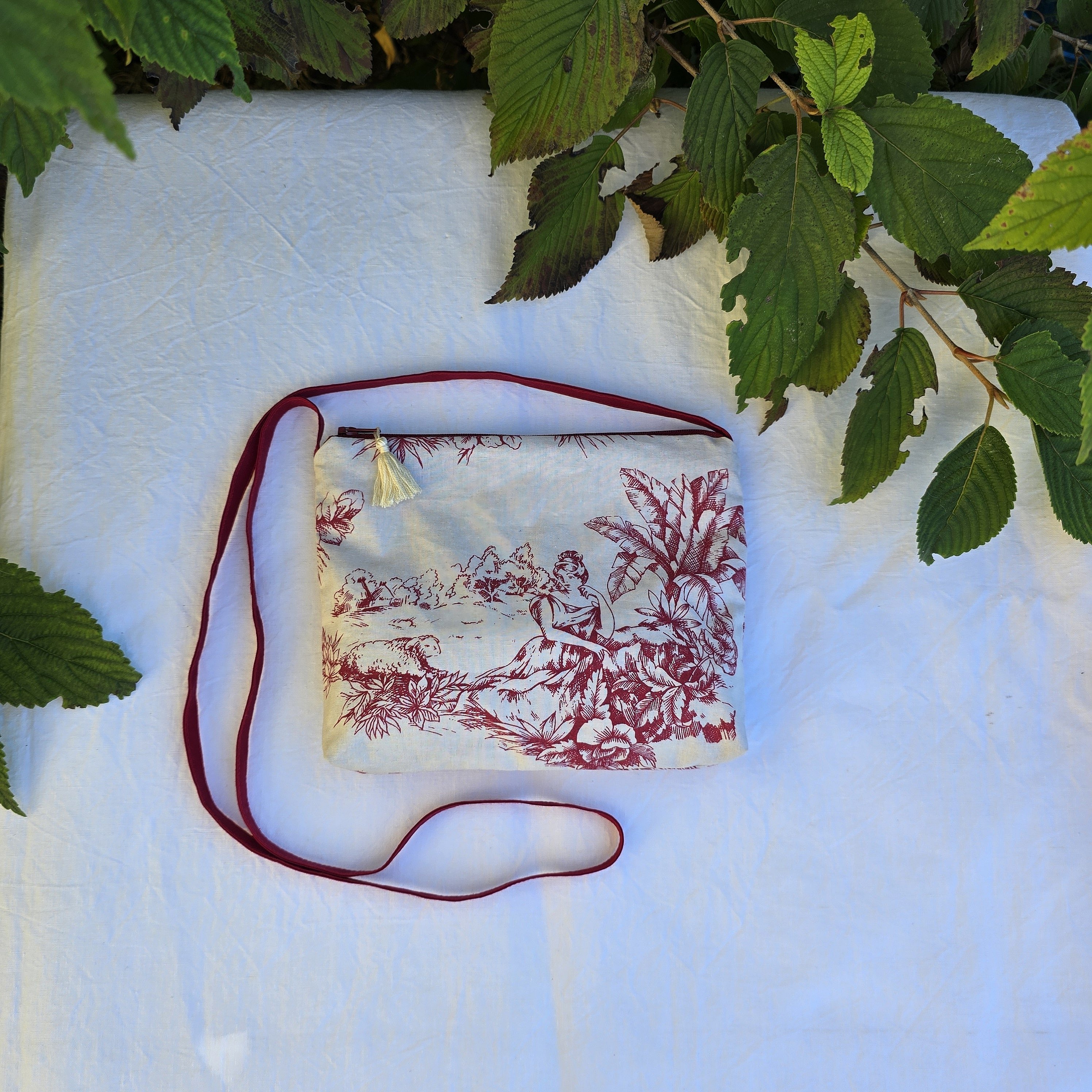 Pochette avec bandouli&egrave;re en tissu toile de Jouy bordeaux et &eacute;cru agr&eacute;ment&eacute;e d'un pompon