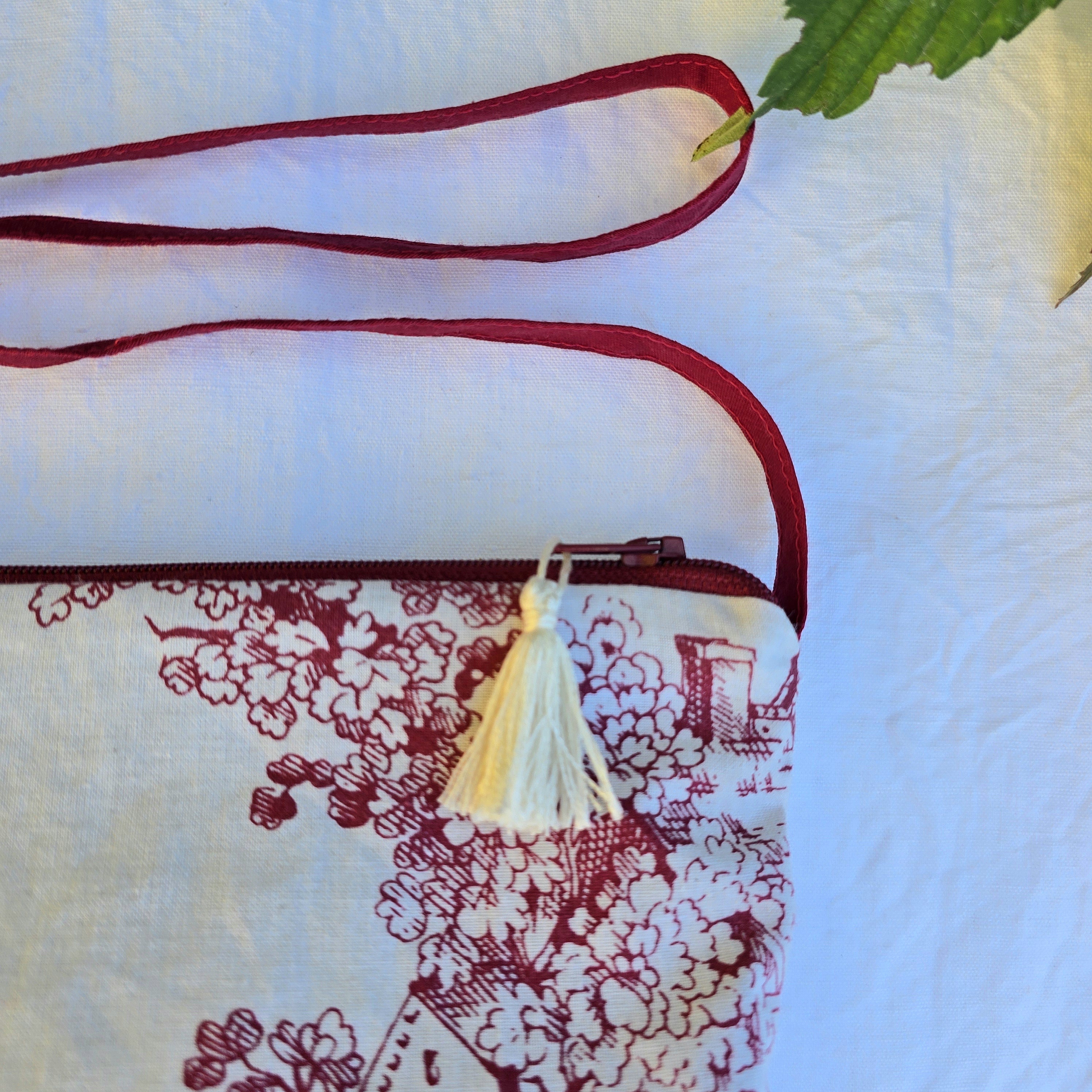 Pochette avec bandouli&egrave;re en tissu toile de Jouy bordeaux et &eacute;cru agr&eacute;ment&eacute;e d'un pompon
