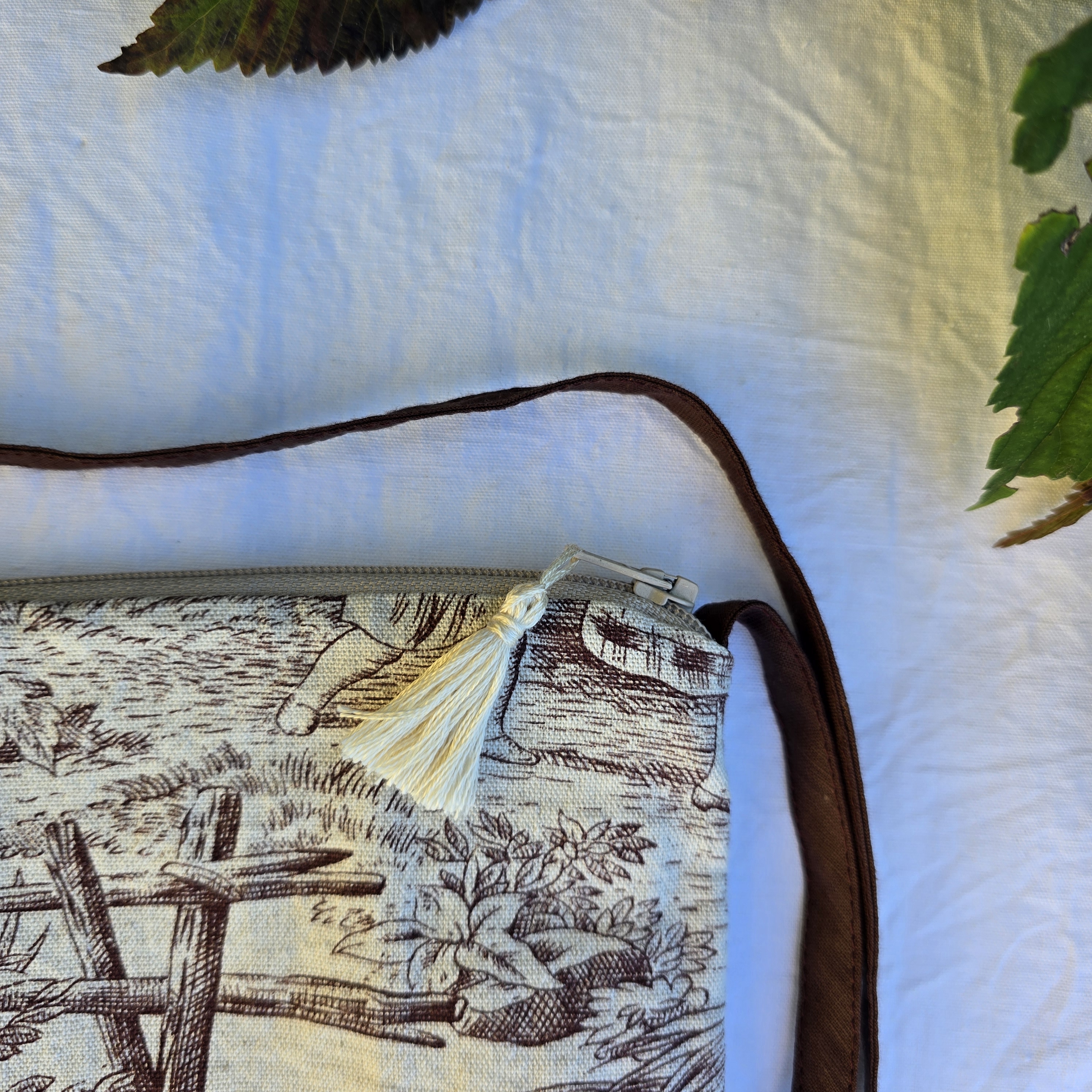 Pochette avec bandouli&egrave;re en tissu toile de Jouy marron et beige agr&eacute;ment&eacute;e d'un pompon