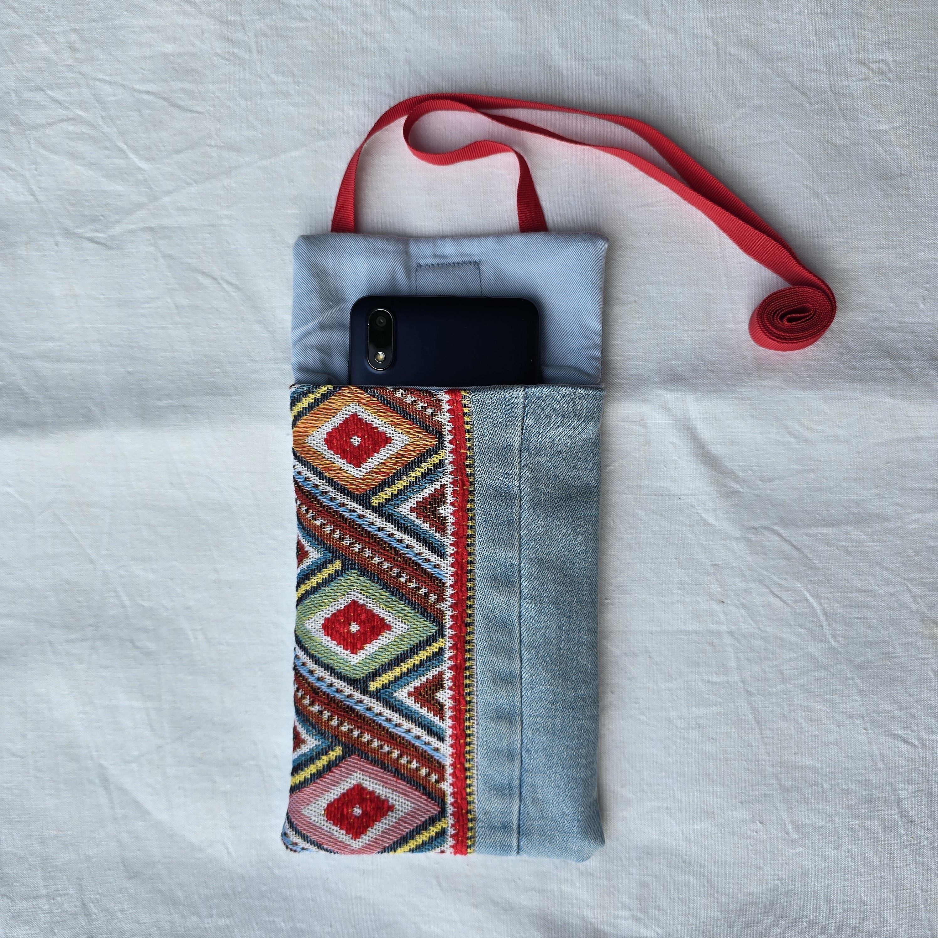 Pochette téléphone en jean recyclé avec bandoulière rouge.