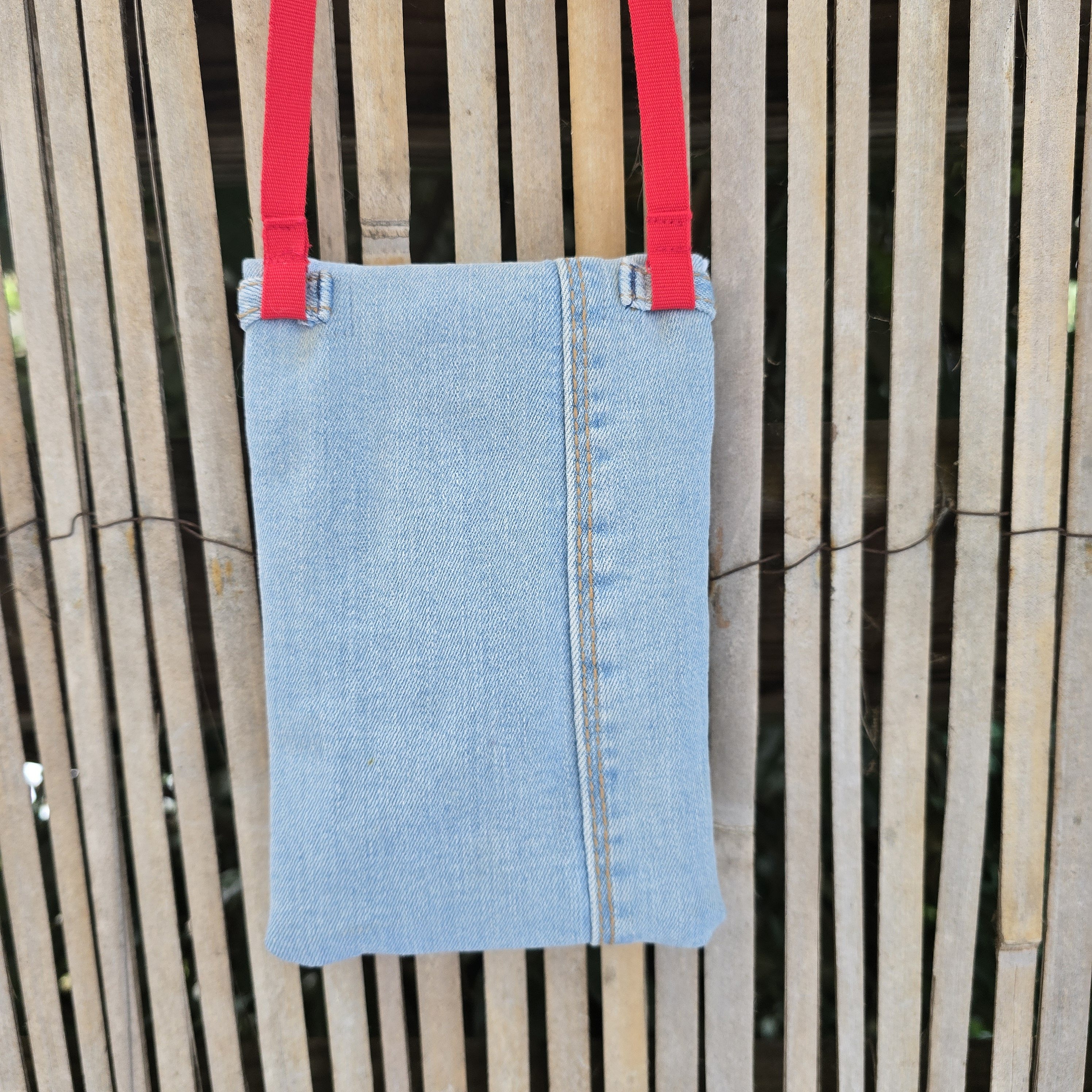 Pochette téléphone en jean recyclé avec bandoulière rouge.