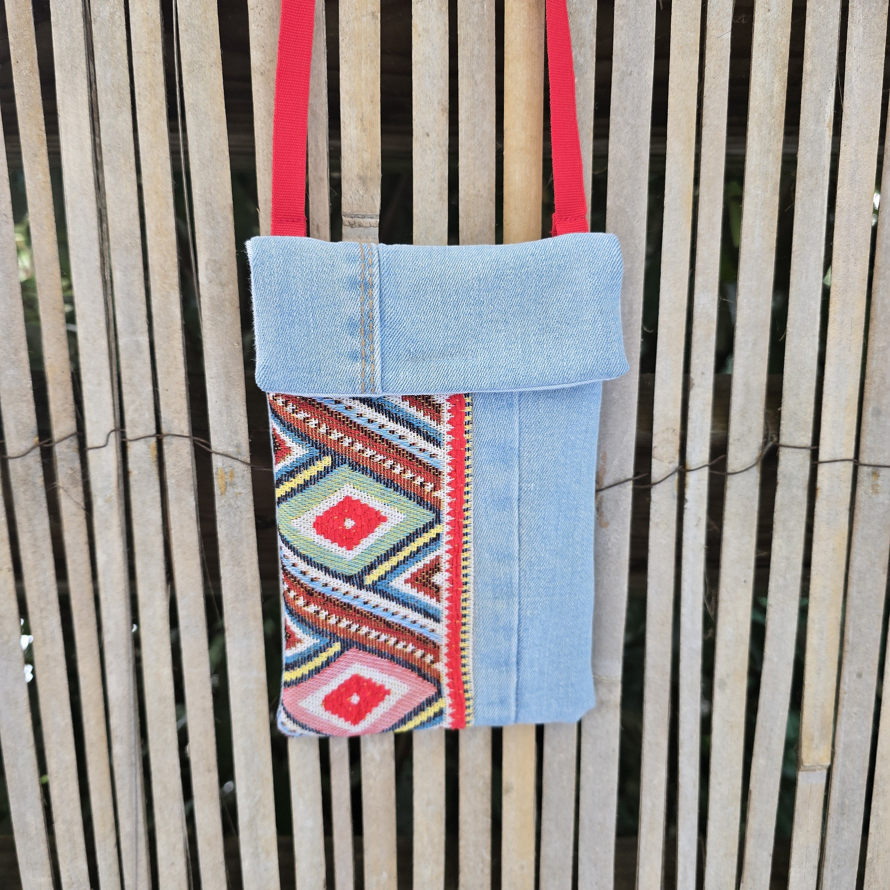 Pochette téléphone en jean recyclé avec bandoulière rouge.
