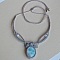 Collier en micro-macram&eacute; gris taupe/bleu givr&eacute; avec en pi&egrave;ce centrale une pierre gemme naturelle aux douces nuances de blanc et de bleu clair.