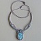 Collier en micro-macram&eacute; gris taupe/bleu givr&eacute; avec en pi&egrave;ce centrale une pierre gemme naturelle aux douces nuances de blanc et de bleu clair.
