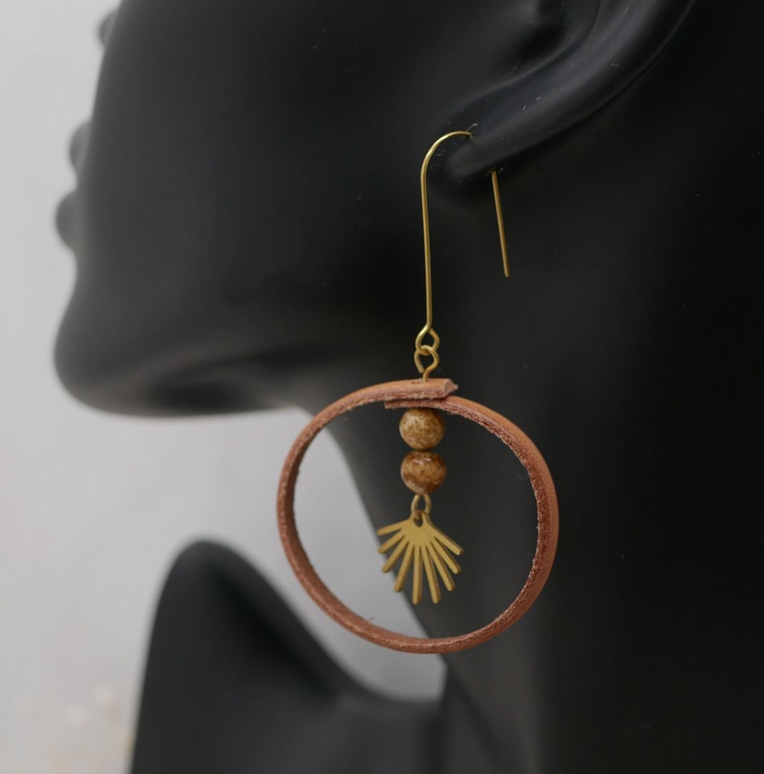 Boucle d'oreille ronde en cuir naturel avec perles dorées.