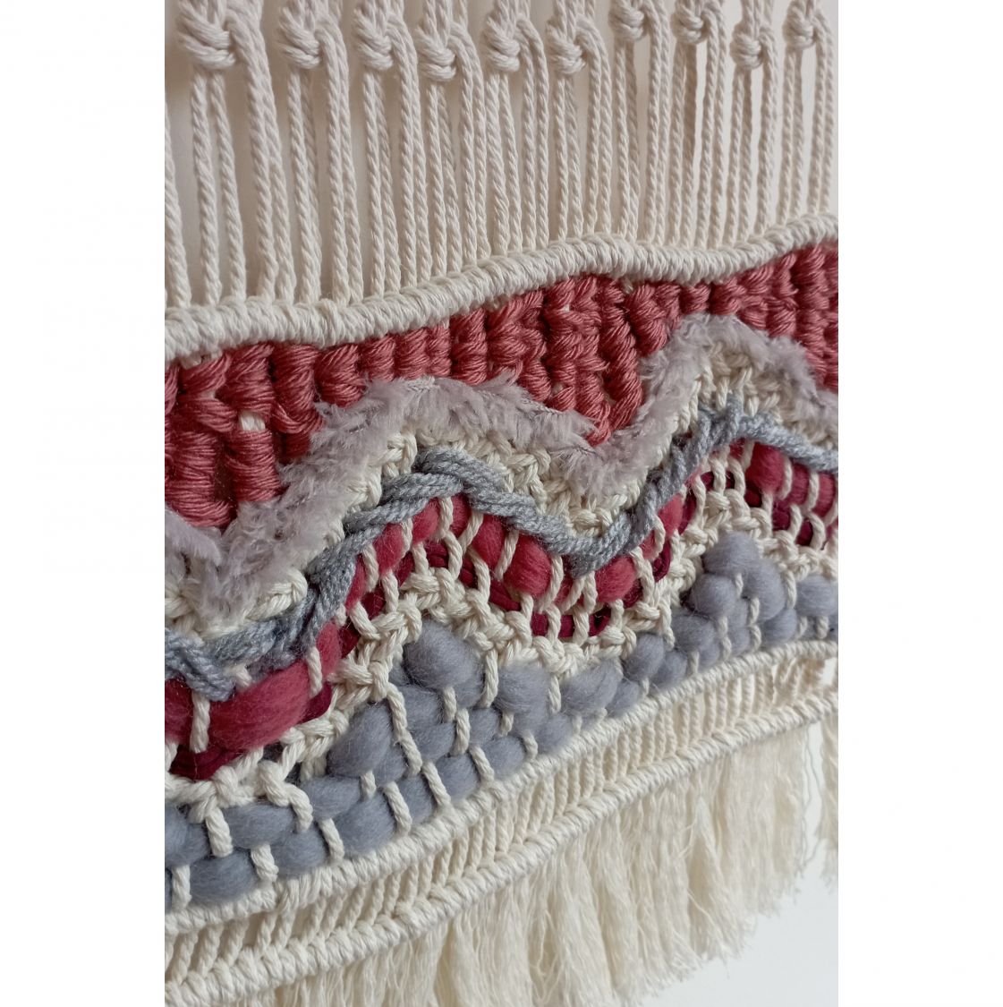 Détail d'une suspension murale artisanale en macramé coloré.