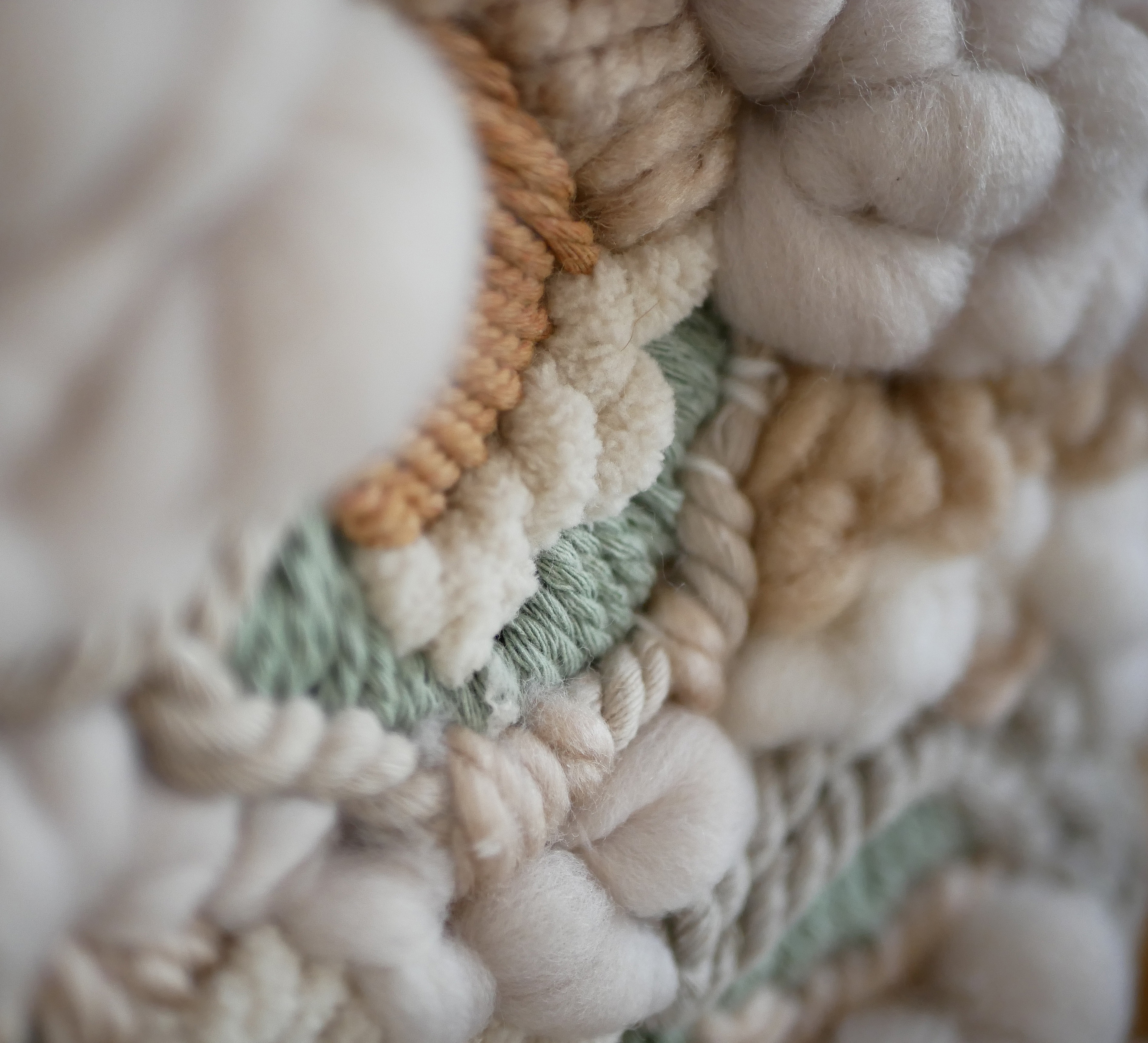 Gros plan sur un tissage mural artisanal en laine beige.