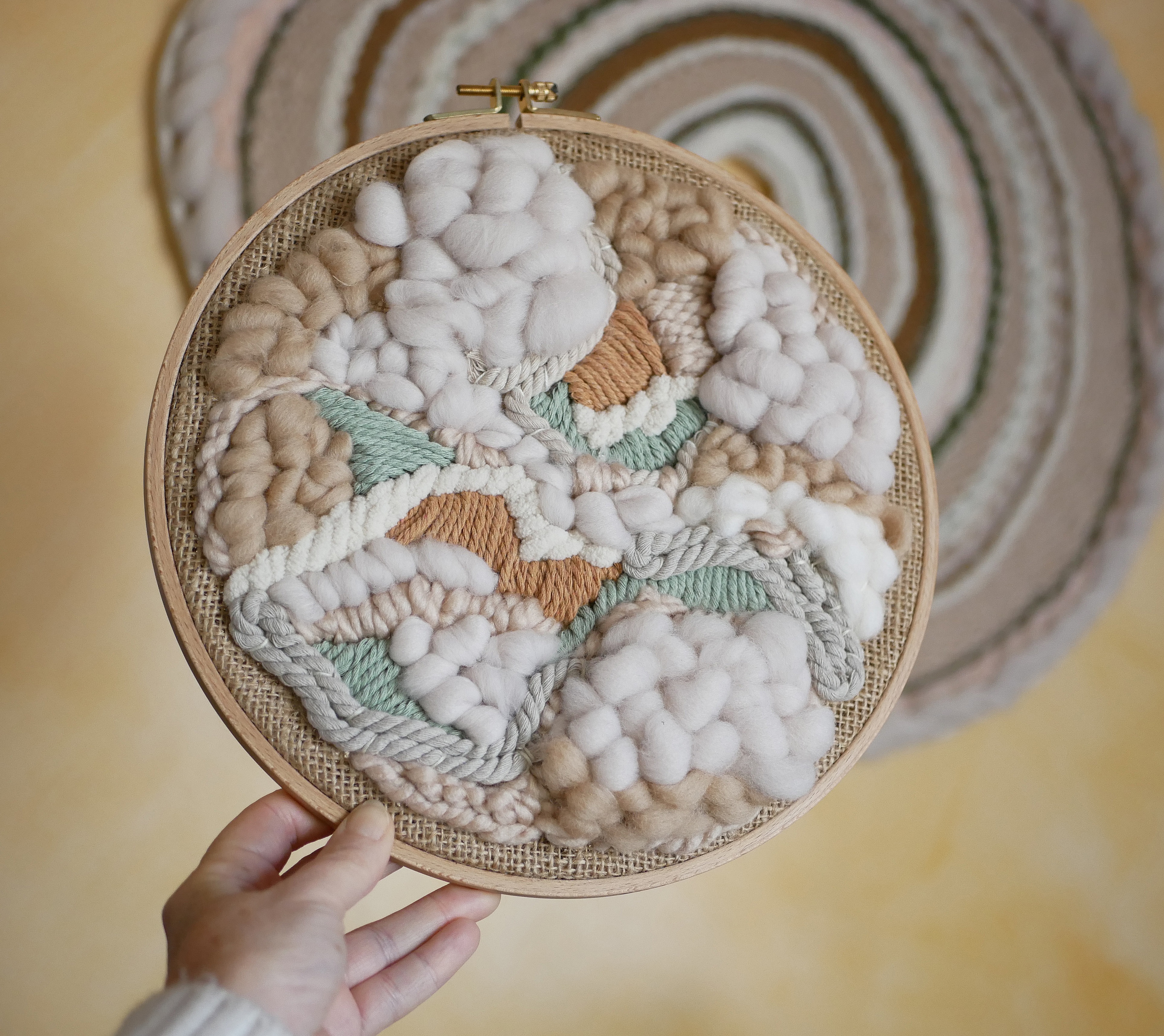 Tissage mural rond en laine et jute, tons beige blanc.