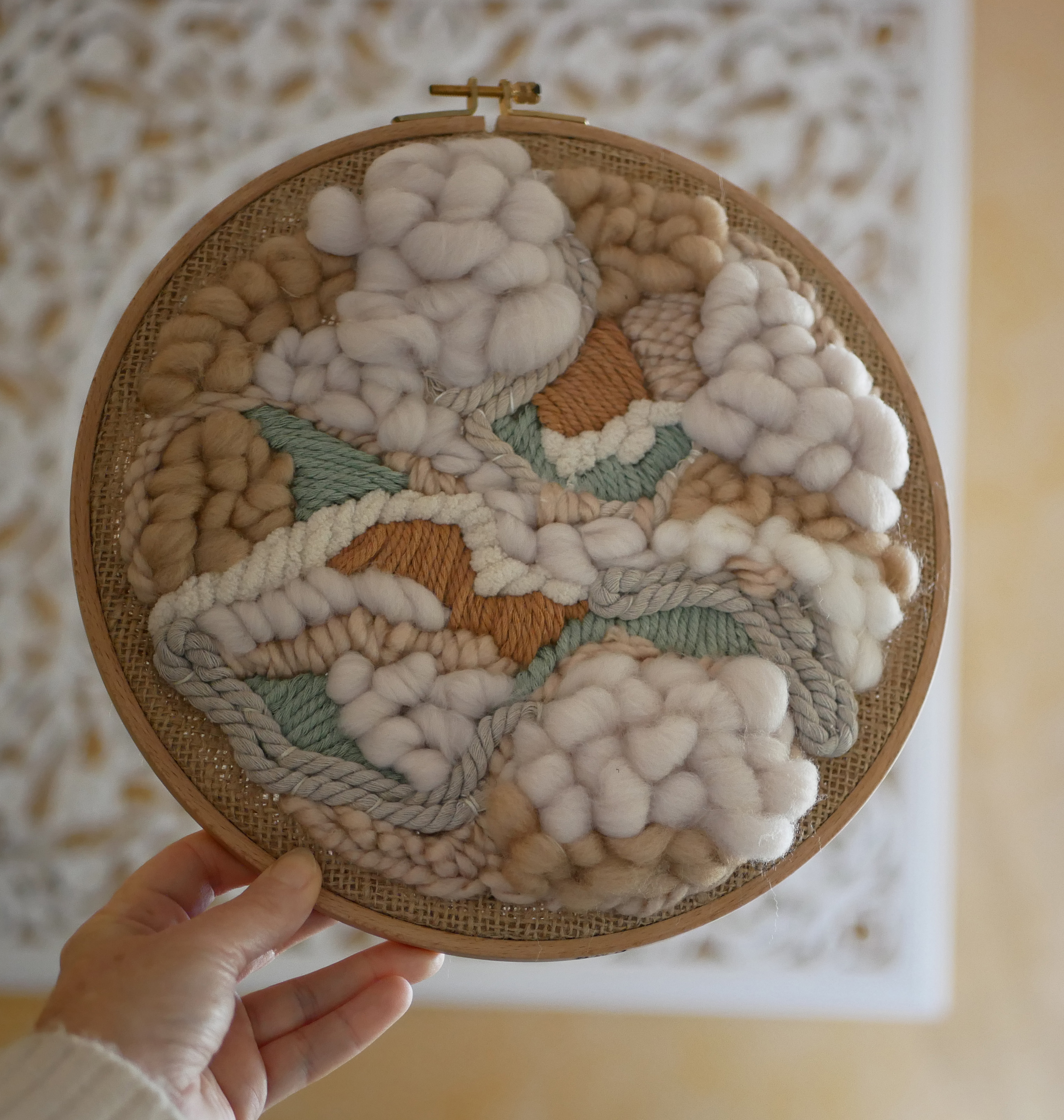 Tissage mural rond en laine et jute, tons beige naturel.