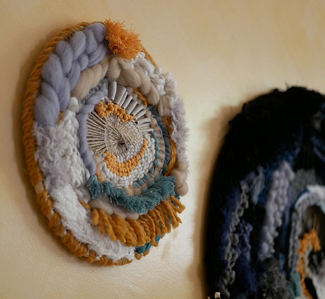 Tissage mural rond contemporain aux textures et pompons colorés.