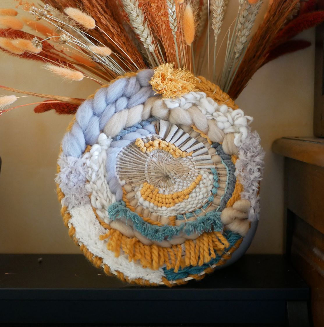 Tissage mural rond contemporain aux textures bohèmes et pompons.