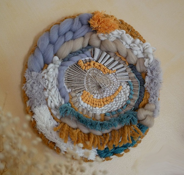 Tissage mural rond contemporain aux textures et pompons bohèmes.