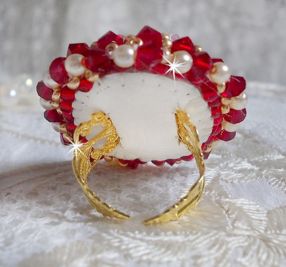 Bague Rubis brod&eacute;e avec un cabochon rectangulaire Ruby, orn&eacute;e de chatons mont&eacute;s en Cristal avec des perles rondes nacr&eacute;es en verre Ivoire, rocailles Dor&eacute;es, des toupies Cristal AB et Burgundy.