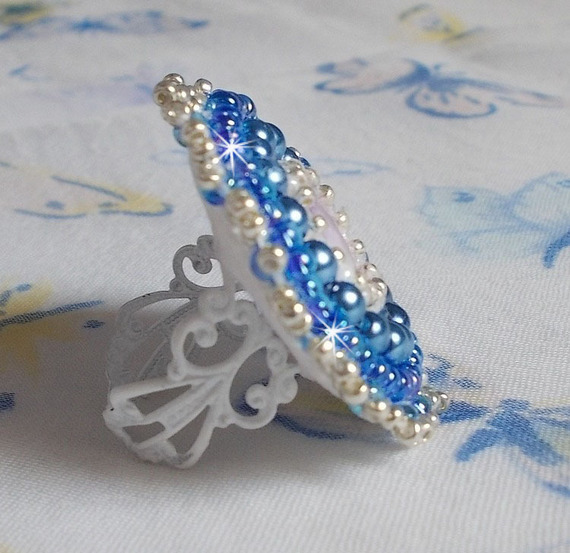 Bague Azur brod&eacute;e avec un cabochon en Cristal de couleur Antique Pink &agrave; laquelle s'ajoute des rocailles et perles rondes nacr&eacute;es. Le tout est mont&eacute; sur une bague filigran&eacute;e Blanche