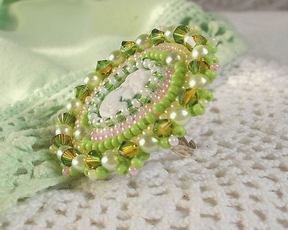 Bague Anisse brod&eacute;e d&rsquo;un cabochon r&eacute;sine repr&eacute;sentant une femme et des roses, orn&eacute;e de rocailles Vert Anis, Rose, Jaune Nacr&eacute; et Ivoire. Elle est finie avec des toupies et perles sur bague r&eacute;glable 