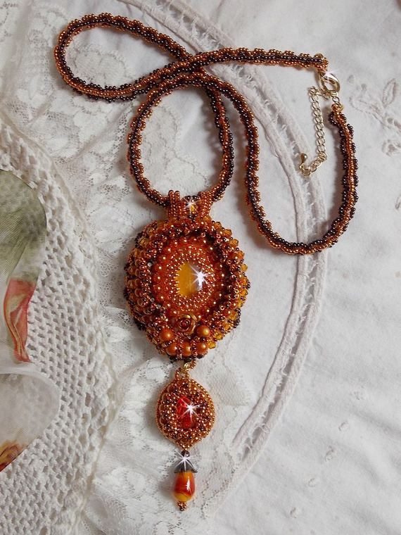Pendentif brodé orange et doré avec perles et cabochon.
