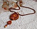 Pendentif brodé artisanal aux perles orange et tons dorés.