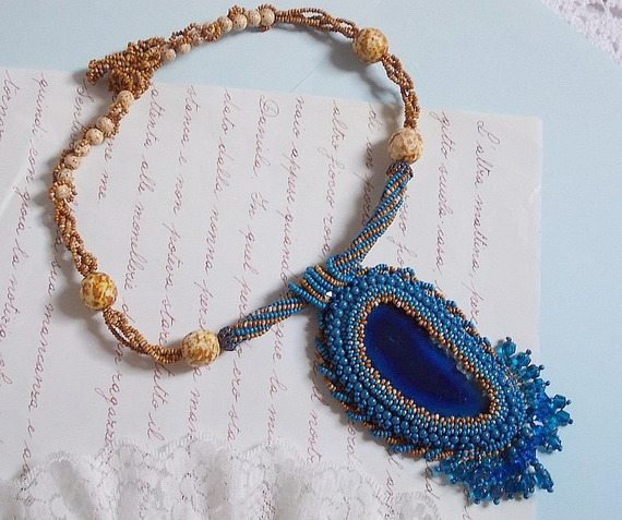 Pendentif Corsica avec un cabochon : une Agate Bleue brod&eacute;e avec des perles nacr&eacute;es Bleu Lapis en cristal &agrave; laquelle s&rsquo;ajoute des rocailles saphir et travertin entrelac&eacute;es pour former une dentelle