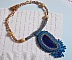 Pendentif Corsica avec un cabochon : une Agate Bleue brod&eacute;e avec des perles nacr&eacute;es Bleu Lapis en cristal &agrave; laquelle s&rsquo;ajoute des rocailles saphir et travertin entrelac&eacute;es pour former une dentelle