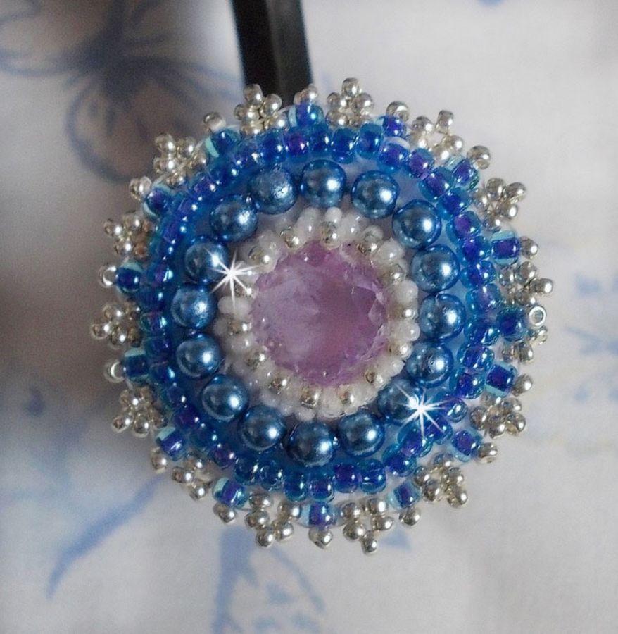 Bague Azur brod&eacute;e avec un cabochon en Cristal de couleur Antique Pink &agrave; laquelle s'ajoute des rocailles et perles rondes nacr&eacute;es. Le tout est mont&eacute; sur une bague filigran&eacute;e Blanche