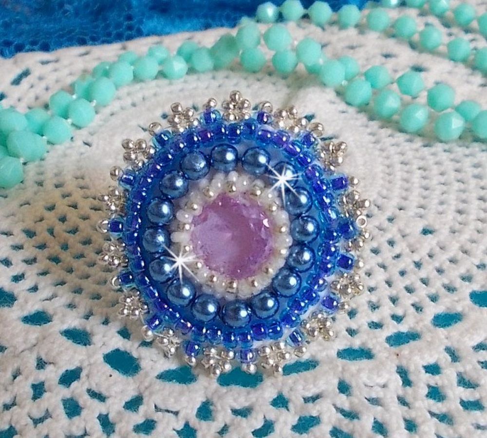 Bague Azur brod&eacute;e avec un cabochon en Cristal de couleur Antique Pink &agrave; laquelle s'ajoute des rocailles et perles rondes nacr&eacute;es. Le tout est mont&eacute; sur une bague filigran&eacute;e Blanche