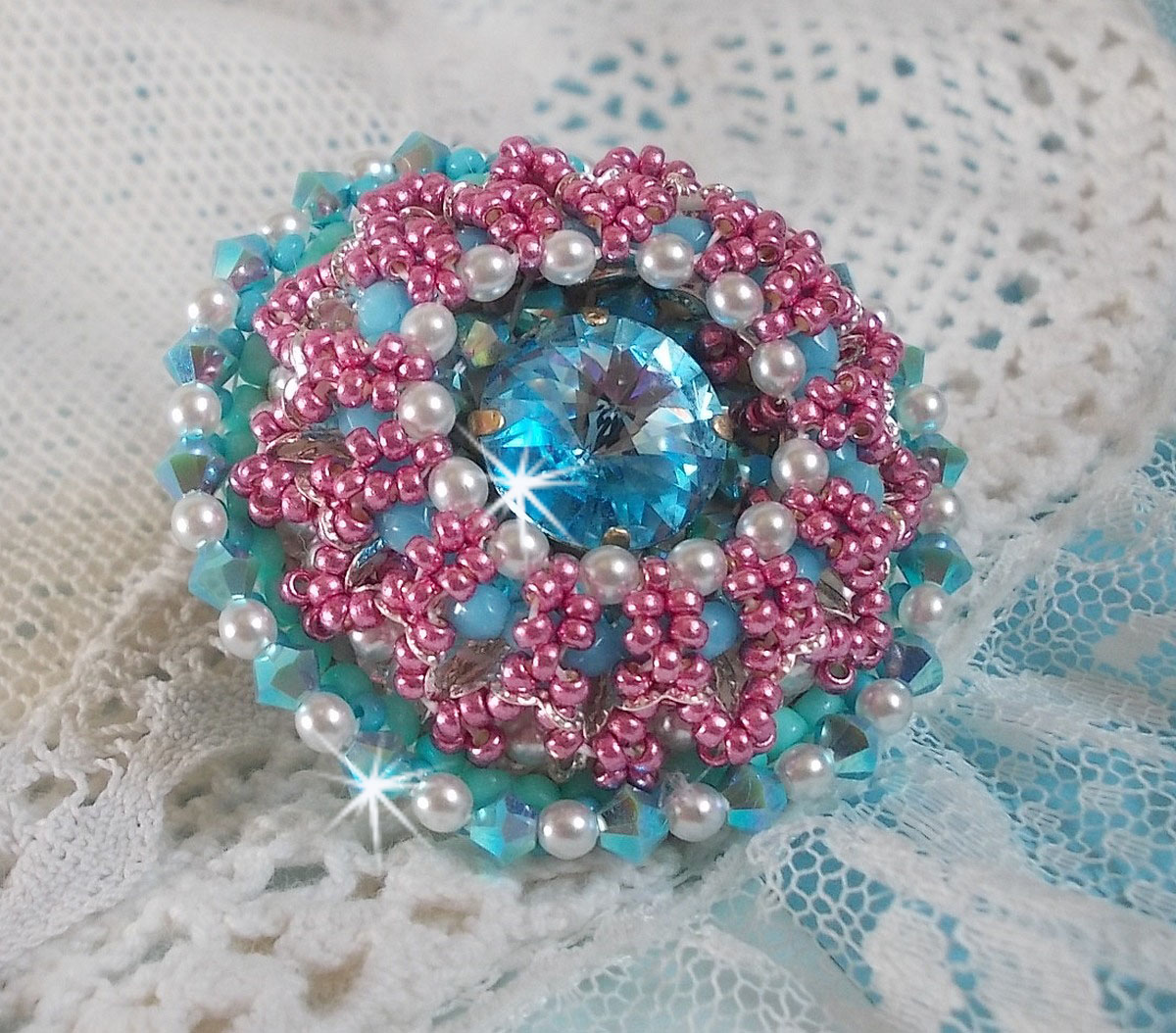 Bague Beauty Alicia Blue brod&eacute;e avec un cabochon en Cristal Bleu, perles nacr&eacute;es Blanches, toupies Turquoises AB2x et rocailles. Le tout est mont&eacute; sur une bague filigran&eacute;e Bleue, un style contemporain