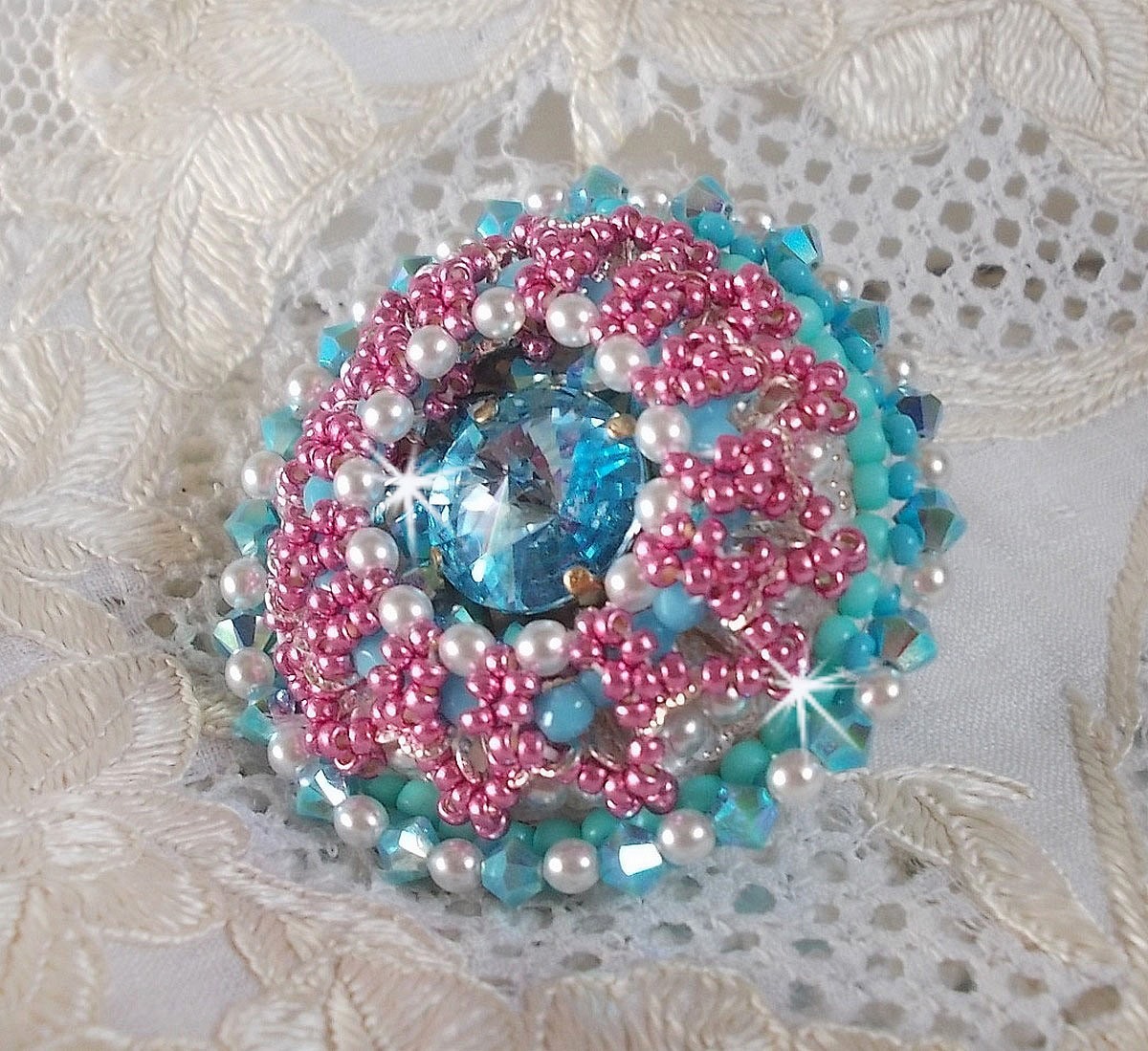 Bague Beauty Alicia Blue brod&eacute;e avec un cabochon en Cristal Bleu, perles nacr&eacute;es Blanches, toupies Turquoises AB2x et rocailles. Le tout est mont&eacute; sur une bague filigran&eacute;e Bleue, un style contemporain