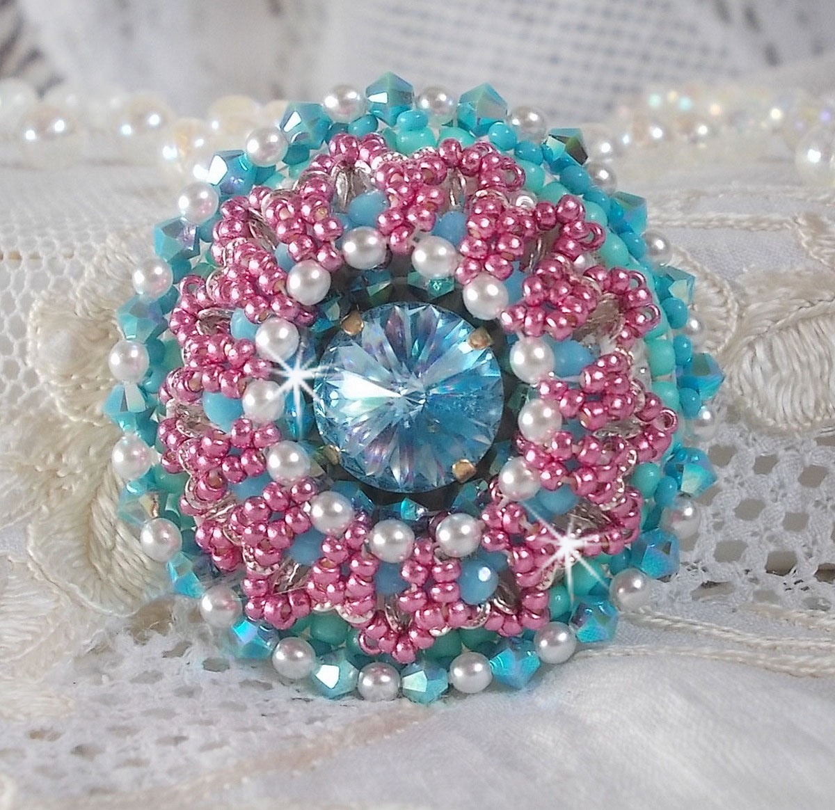 Bague Beauty Alicia Blue brod&eacute;e avec un cabochon en Cristal Bleu, perles nacr&eacute;es Blanches, toupies Turquoises AB2x et rocailles. Le tout est mont&eacute; sur une bague filigran&eacute;e Bleue, un style contemporain