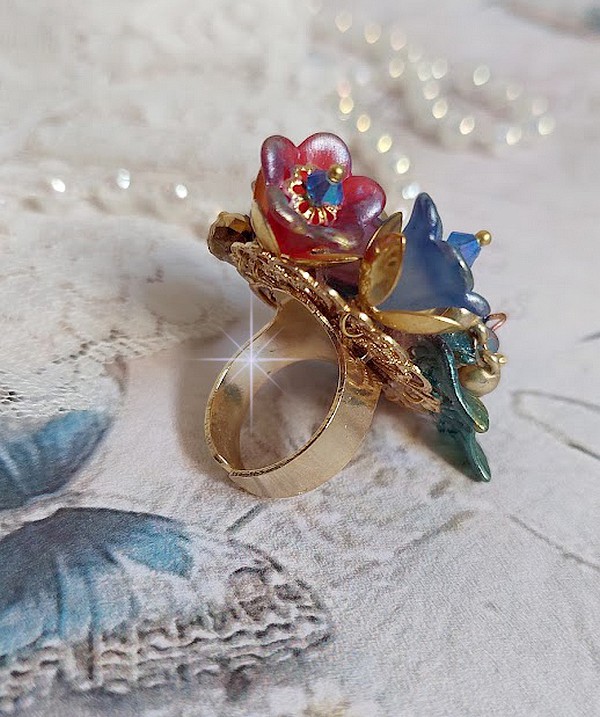 Bague Bel Air mont&eacute;e avec des fleurs lucites peintes &agrave; la main aux couleurs : Bleu, Rose, Rouge, Argent, Blanc avec feuilles ondul&eacute;es Vert Cuivr&eacute; &agrave; laquelle s&rsquo;ajoute perles Dor&eacute;es en Verre