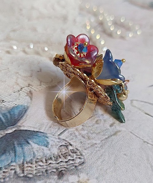 Bague Bel Air mont&eacute;e avec des fleurs lucites peintes &agrave; la main aux couleurs : Bleu, Rose, Rouge, Argent, Blanc avec feuilles ondul&eacute;es Vert Cuivr&eacute; &agrave; laquelle s&rsquo;ajoute perles Dor&eacute;es en Verre