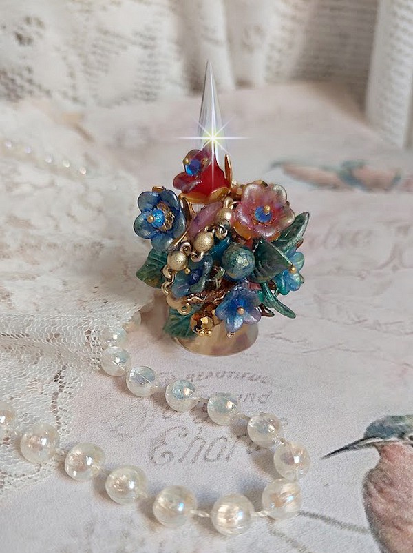 Bague Bel Air mont&eacute;e avec des fleurs lucites peintes &agrave; la main aux couleurs : Bleu, Rose, Rouge, Argent, Blanc avec feuilles ondul&eacute;es Vert Cuivr&eacute; &agrave; laquelle s&rsquo;ajoute perles Dor&eacute;es en Verre