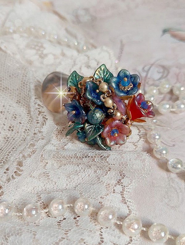 Bague Bel Air mont&eacute;e avec des fleurs lucites peintes &agrave; la main aux couleurs : Bleu, Rose, Rouge, Argent, Blanc avec feuilles ondul&eacute;es Vert Cuivr&eacute; &agrave; laquelle s&rsquo;ajoute perles Dor&eacute;es en Verre