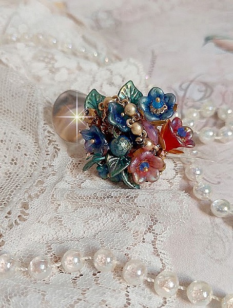 Bague Bel Air mont&eacute;e avec des fleurs lucites peintes &agrave; la main aux couleurs : Bleu, Rose, Rouge, Argent, Blanc avec feuilles ondul&eacute;es Vert Cuivr&eacute; &agrave; laquelle s&rsquo;ajoute perles Dor&eacute;es en Verre