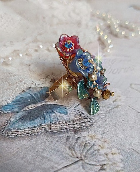 Bague Bel Air mont&eacute;e avec des fleurs lucites peintes &agrave; la main aux couleurs : Bleu, Rose, Rouge, Argent, Blanc avec feuilles ondul&eacute;es Vert Cuivr&eacute; &agrave; laquelle s&rsquo;ajoute perles Dor&eacute;es en Verre