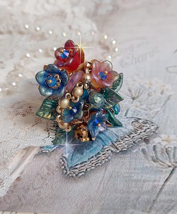Bague Bel Air mont&eacute;e avec des fleurs lucites peintes &agrave; la main aux couleurs : Bleu, Rose, Rouge, Argent, Blanc avec feuilles ondul&eacute;es Vert Cuivr&eacute; &agrave; laquelle s&rsquo;ajoute perles Dor&eacute;es en Verre