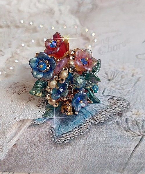 Bague Bel Air mont&eacute;e avec des fleurs lucites peintes &agrave; la main aux couleurs : Bleu, Rose, Rouge, Argent, Blanc avec feuilles ondul&eacute;es Vert Cuivr&eacute; &agrave; laquelle s&rsquo;ajoute perles Dor&eacute;es en Verre