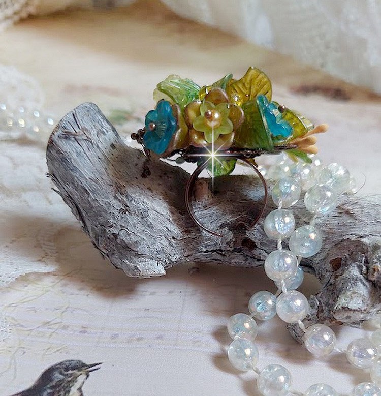 Bague C&eacute;zanne mont&eacute;e avec des petites fleurs lucites peintes &agrave; la main &agrave; laquelle s&rsquo;ajoute des feuilles, cristaux, perles, &eacute;tamines, grosses rocailles, perles nacr&eacute;es et m&eacute;tal sur une bague en Laiton