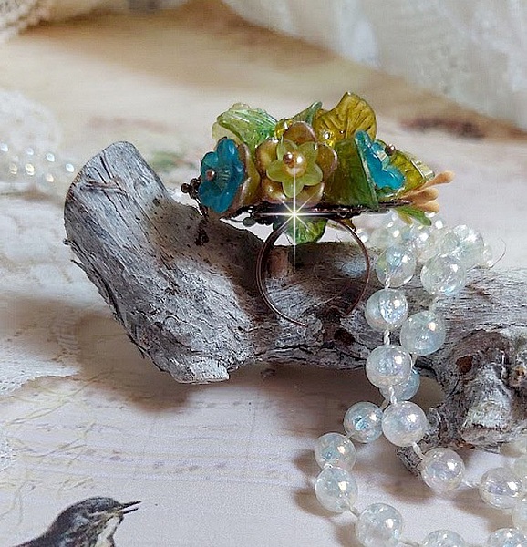 Bague C&eacute;zanne mont&eacute;e avec des petites fleurs lucites peintes &agrave; la main &agrave; laquelle s&rsquo;ajoute des feuilles, cristaux, perles, &eacute;tamines, grosses rocailles, perles nacr&eacute;es et m&eacute;tal sur une bague en Laiton