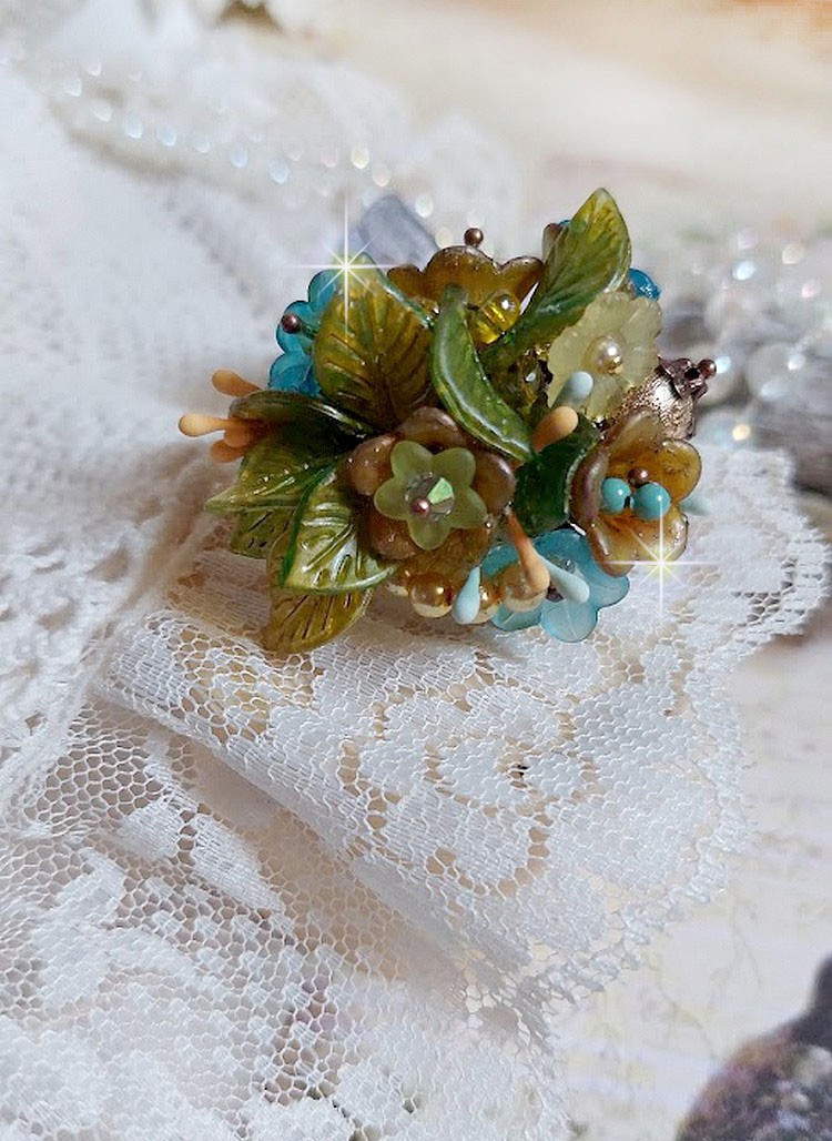 Bague C&eacute;zanne mont&eacute;e avec des petites fleurs lucites peintes &agrave; la main &agrave; laquelle s&rsquo;ajoute des feuilles, cristaux, perles, &eacute;tamines, grosses rocailles, perles nacr&eacute;es et m&eacute;tal sur une bague en Laiton