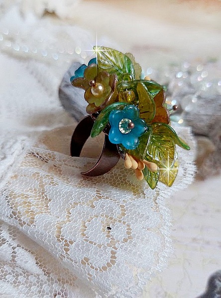 Bague C&eacute;zanne mont&eacute;e avec des petites fleurs lucites peintes &agrave; la main &agrave; laquelle s&rsquo;ajoute des feuilles, cristaux, perles, &eacute;tamines, grosses rocailles, perles nacr&eacute;es et m&eacute;tal sur une bague en Laiton