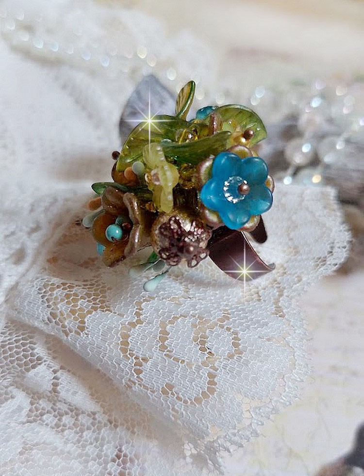 Bague C&eacute;zanne mont&eacute;e avec des petites fleurs lucites peintes &agrave; la main &agrave; laquelle s&rsquo;ajoute des feuilles, cristaux, perles, &eacute;tamines, grosses rocailles, perles nacr&eacute;es et m&eacute;tal sur une bague en Laiton