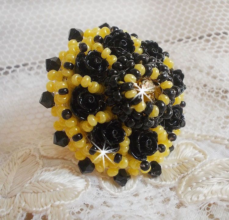 Bague Dorine brod&eacute;e avec un chaton Cristal/Dor&eacute; orn&eacute;e de roses en R&eacute;sine Noire &agrave; laquelle s&rsquo;ajoute des rocailles Jaunes et Jet mont&eacute;es en D&ocirc;me. L&rsquo;arri&egrave;re est en cuir vachette sur une bague Laiton