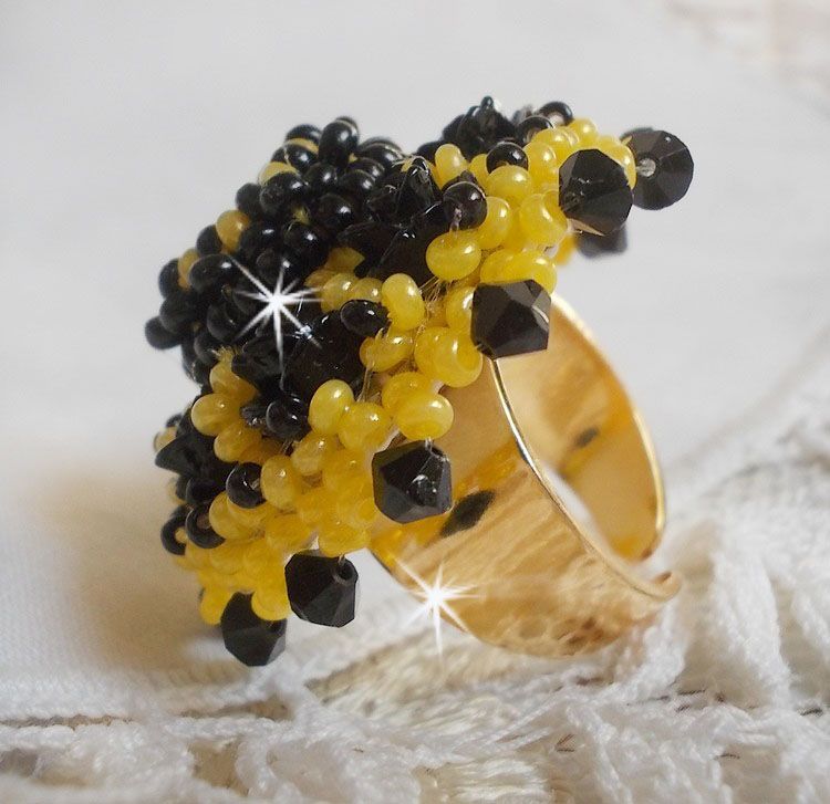Bague Dorine brod&eacute;e avec un chaton Cristal/Dor&eacute; orn&eacute;e de roses en R&eacute;sine Noire &agrave; laquelle s&rsquo;ajoute des rocailles Jaunes et Jet mont&eacute;es en D&ocirc;me. L&rsquo;arri&egrave;re est en cuir vachette sur une bague Laiton