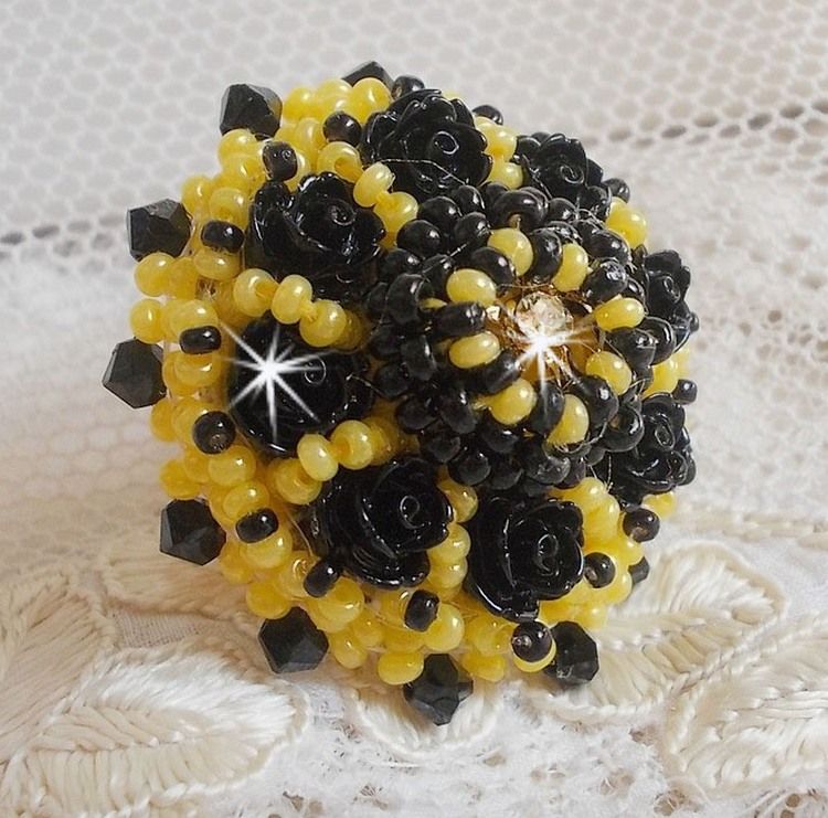 Bague Dorine brod&eacute;e avec un chaton Cristal/Dor&eacute; orn&eacute;e de roses en R&eacute;sine Noire &agrave; laquelle s&rsquo;ajoute des rocailles Jaunes et Jet mont&eacute;es en D&ocirc;me. L&rsquo;arri&egrave;re est en cuir vachette sur une bague Laiton