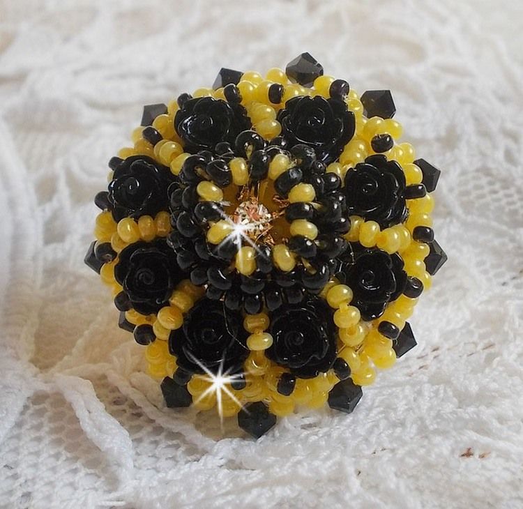 Bague Dorine brod&eacute;e avec un chaton Cristal/Dor&eacute; orn&eacute;e de roses en R&eacute;sine Noire &agrave; laquelle s&rsquo;ajoute des rocailles Jaunes et Jet mont&eacute;es en D&ocirc;me. L&rsquo;arri&egrave;re est en cuir vachette sur une bague Laiton