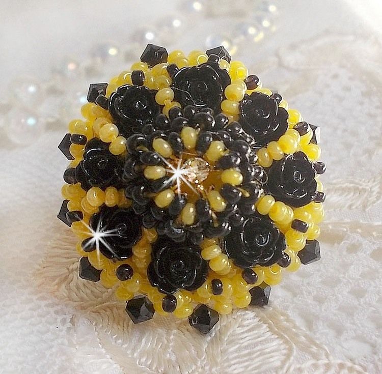 Bague Dorine brod&eacute;e avec un chaton Cristal/Dor&eacute; orn&eacute;e de roses en R&eacute;sine Noire &agrave; laquelle s&rsquo;ajoute des rocailles Jaunes et Jet mont&eacute;es en D&ocirc;me. L&rsquo;arri&egrave;re est en cuir vachette sur une bague Laiton