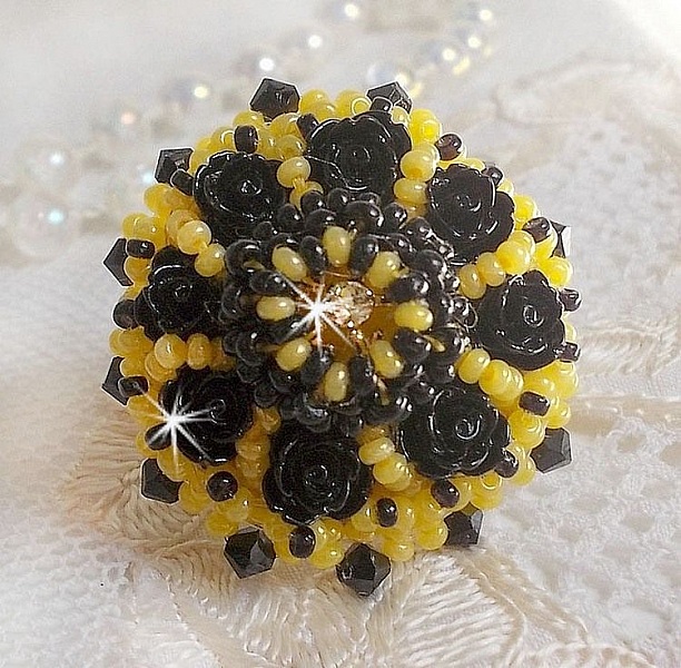 Bague Dorine brod&eacute;e avec un chaton Cristal/Dor&eacute; orn&eacute;e de roses en R&eacute;sine Noire &agrave; laquelle s&rsquo;ajoute des rocailles Jaunes et Jet mont&eacute;es en D&ocirc;me. L&rsquo;arri&egrave;re est en cuir vachette sur une bague Laiton