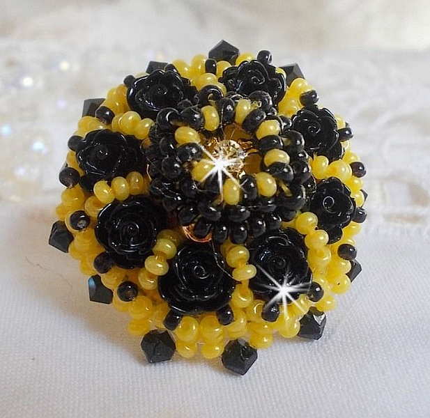 Bague Dorine brod&eacute;e avec un chaton Cristal/Dor&eacute; orn&eacute;e de roses en R&eacute;sine Noire &agrave; laquelle s&rsquo;ajoute des rocailles Jaunes et Jet mont&eacute;es en D&ocirc;me. L&rsquo;arri&egrave;re est en cuir vachette sur une bague Laiton