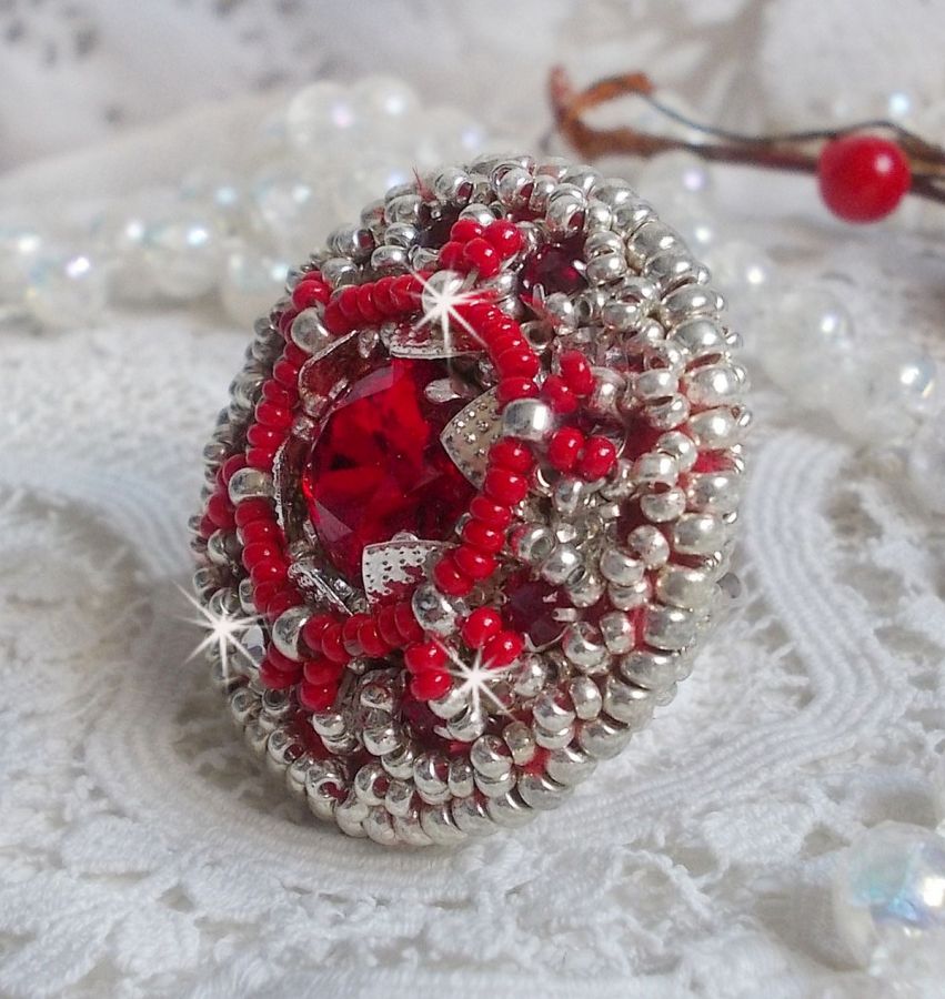 Bague Drigon Red brod&eacute;e avec un cabochon carr&eacute; Rouge sur une estampe Argent&eacute;e. Orn&eacute;e de chatons en Cristal puis model&eacute;e avec des rocailles et perles. Le tout est mont&eacute; sur une bague r&eacute;glable argent&eacute;e 